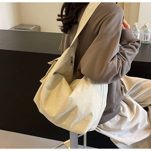 Detailed view of beige slouchy crossbody bag in textured fabric on model's shoulder