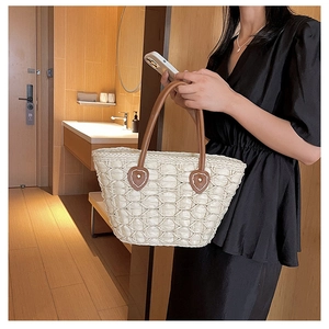 Detail of woven straw tote bag featuring brown leather handles and reinforced shield decor