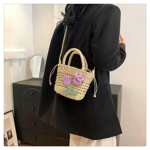 Fashionable beige straw crossbody bag with purple crochet flowers on a casual female model