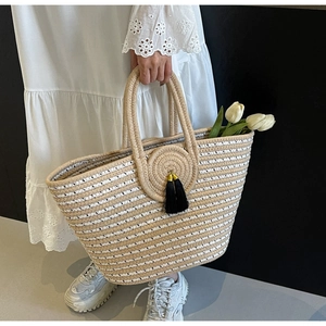 Detail of woven tote bag featuring beige stripes, circular floral patterns and black tassels