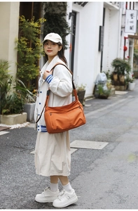 Detail of orange nylon crossbody bag with dual zip pockets shown in street style scene