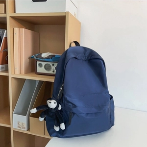 Simple navy blue nylon backpack with monkey keychain in a minimalist home setting