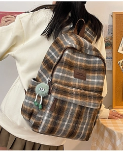 Détail du sac à dos en laine à carreaux avec logo en cuir et breloque pelucheuse