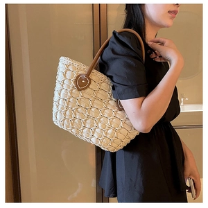 Detailed view of woven tote bag with brown leather handles and heart stitching accents
