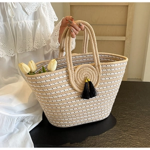 Detail of hand-woven rope tote bag with circular ornament and black tassels on white lace top