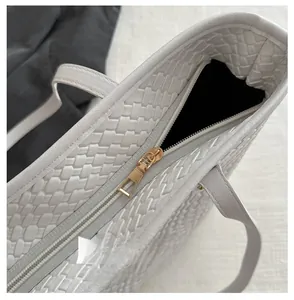 Gros plan sur la fermeture éclair dorée et la texture tressée du sac blanc en PU