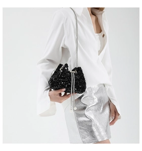 Detail view of black sequin bucket bag with silver chain strap and pearl drawstring tassels