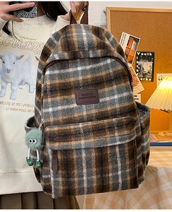 Gros plan du sac à dos en peluche à carreaux marron avec écusson en cuir et breloque verte