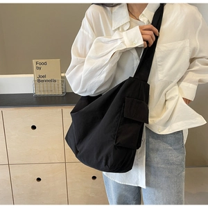 Detail shot of wide shoulder strap and small utility pocket on black nylon crossbody bag