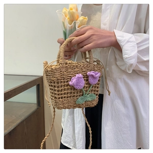 Detail of hand-woven straw crossbody bag featuring purple crochet tulips and drawstring liner