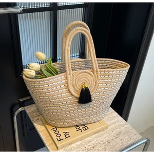 Minimalist woven handbag with beige stripes and black tassels on marble background