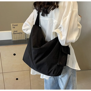 Detailed view of black canvas crossbody bag with wide shoulder strap worn by a model