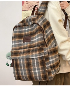 Détail d'un sac à dos en peluche à carreaux avec patch logo en cuir et pendentif monstre