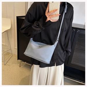 Close-up of light blue minimalist nylon crossbody bag worn by model with white skirt