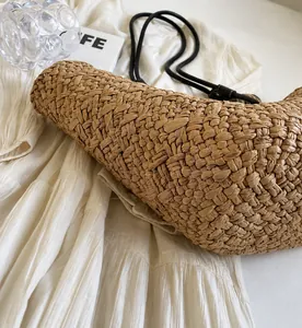 Gros plan sur la texture en paille tressée naturelle et la fine bandoulière noire du sac