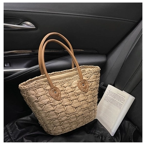 Handwoven beige tote bag with brown leather handles placed on a black leather car seat