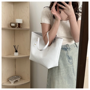Détail d'un sac cabas tissé blanc avec ferrures dorées porté par un mannequin en intérieur