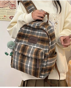 Détail d'un sac à dos en laine à carreaux marron avec peluche monstre verte et logo