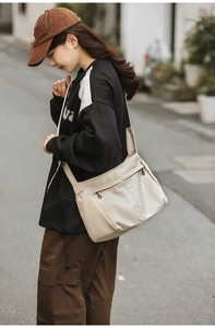 Detail of cream nylon messenger bag with front zipper pocket and adjustable side straps