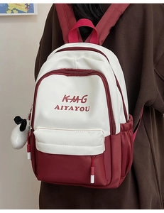 Detail of red and white backpack featuring letter print and cute plush animal charm
