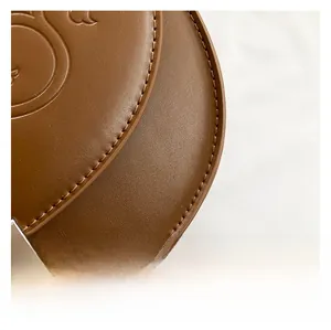 Détail macro du sac en cuir marron avec coutures fines et logo de taureau embossé
