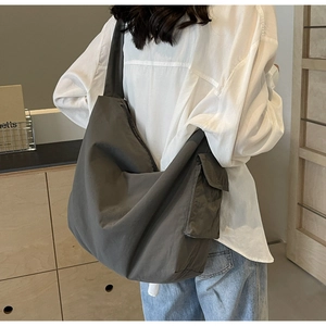 Detail of grey canvas crossbody bag with wide strap and side pocket on a female model