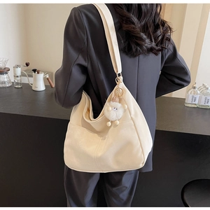 Detail of cream crossbody bag with wide strap and plush pendant in a cafe setting