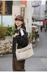 Detail of a beige nylon crossbody bag featuring multiple zipper pockets and black hook accents