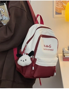 Detail of color-block backpack in cream and red with cute plush dog pendant accessory