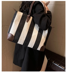 Dettaglio della borsa tote in tela a righe con manici in pelle marrone su una modella