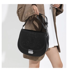 Détail du sac selle en cuir PU noir avec motif circulaire embossé et boucles argentées