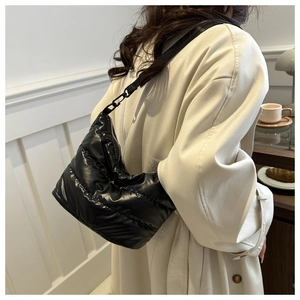 Detail of a black quilted down bag with shiny nylon texture worn by a model in a cafe