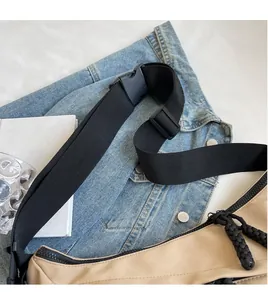 Detail of adjustable black woven shoulder strap with plastic buckle on a beige nylon bag