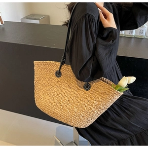 Détail de la texture d'un cabas en paille tressée avec anse en cuir noir et anneaux