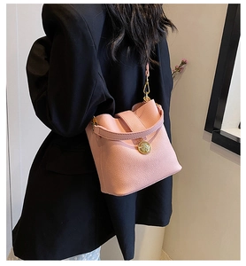 Détail du sac seau en cuir grainé rose avec emblème doré et bandoulière assortie