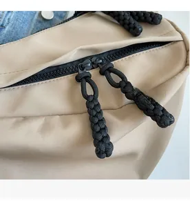 Close-up of dual black woven rope zipper pulls on a beige minimalist fabric crossbody bag