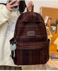 Détail du sac à dos à carreaux avec logo en cuir marron et porte-clé monstre en peluche