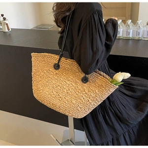Détail du sac cabas en paille tissée avec bandoulières en cuir noir sur un mannequin