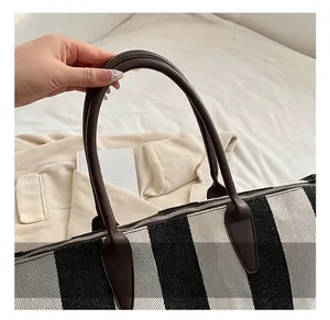 Dettaglio di una borsa tote a righe bianche e nere con manici in pelle marrone e cuciture forti