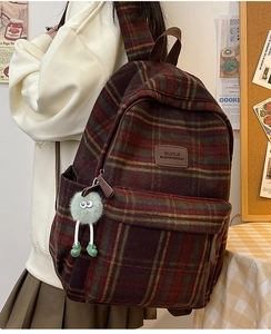 Vue détaillée du sac à dos à carreaux rouges avec logo en cuir et charm monstre vert