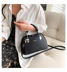 Détail d'un sac coquille noir en cuir grainé avec fermeture éclair argentée et logo