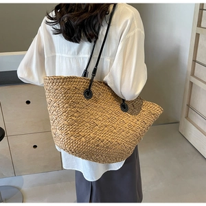 Détail d'un sac cabas en paille tressée avec texture naturelle et fine bandoulière noire