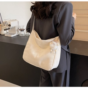 Chic cream hobo bag with plush lamb charm shown on shoulder in a minimalist cafe