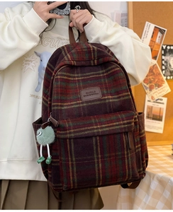 Vue détaillée d'un sac à dos en laine à carreaux rouge et vert avec charm et logo en cuir