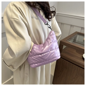 Detail of lavender puffer crossbody bag with metallic sheen worn over an off-white coat