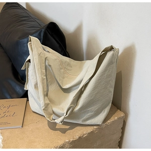 Minimalist large beige nylon crossbody hobo bag displayed on a stone surface