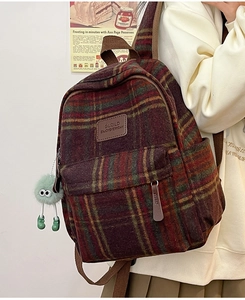Gros plan du sac à dos en nylon écossais avec écusson en cuir et charm boule de poil