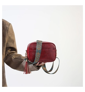 Detail of red PU leather bag featuring a colorful bohemian woven strap and side tassel