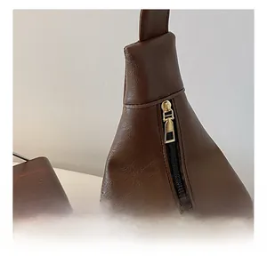 Close-up of smooth gold metal zipper on dark brown faux leather bag with lychee texture