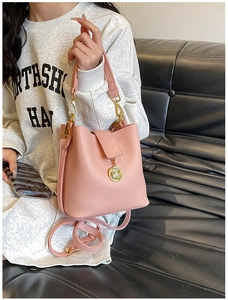 Détail du sac seau rose avec texture litchi, finitions dorées et pendentif en métal